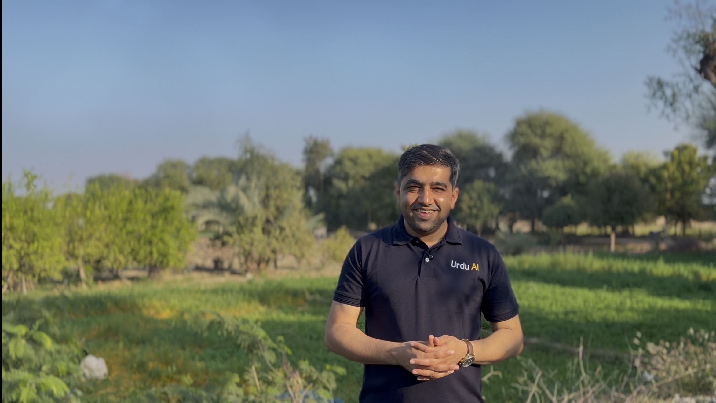 Qaisar Roonjha standing in green fields, wearing an Urdu AI polo shirt